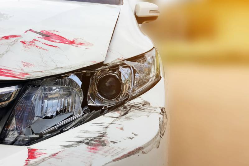 Damaged white car headlight and fender with scratches.