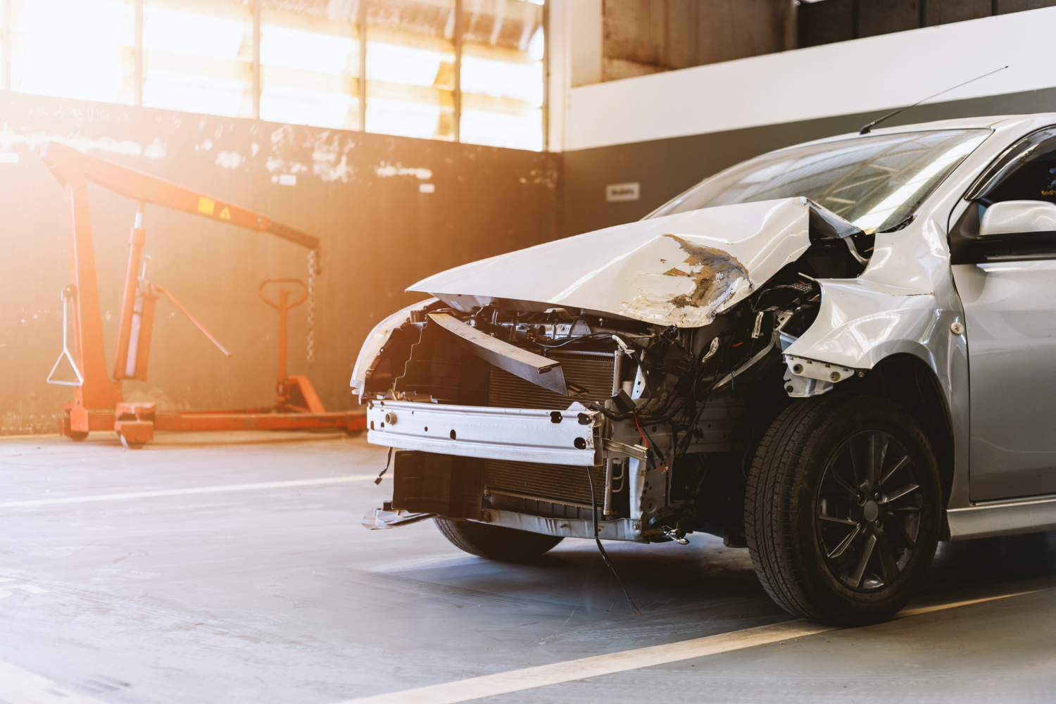 Damaged silver car in auto body shop.