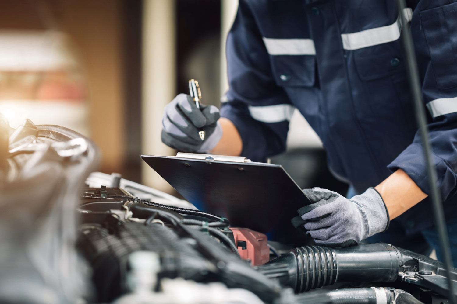 Mechanic inspecting car engine with clipboard.