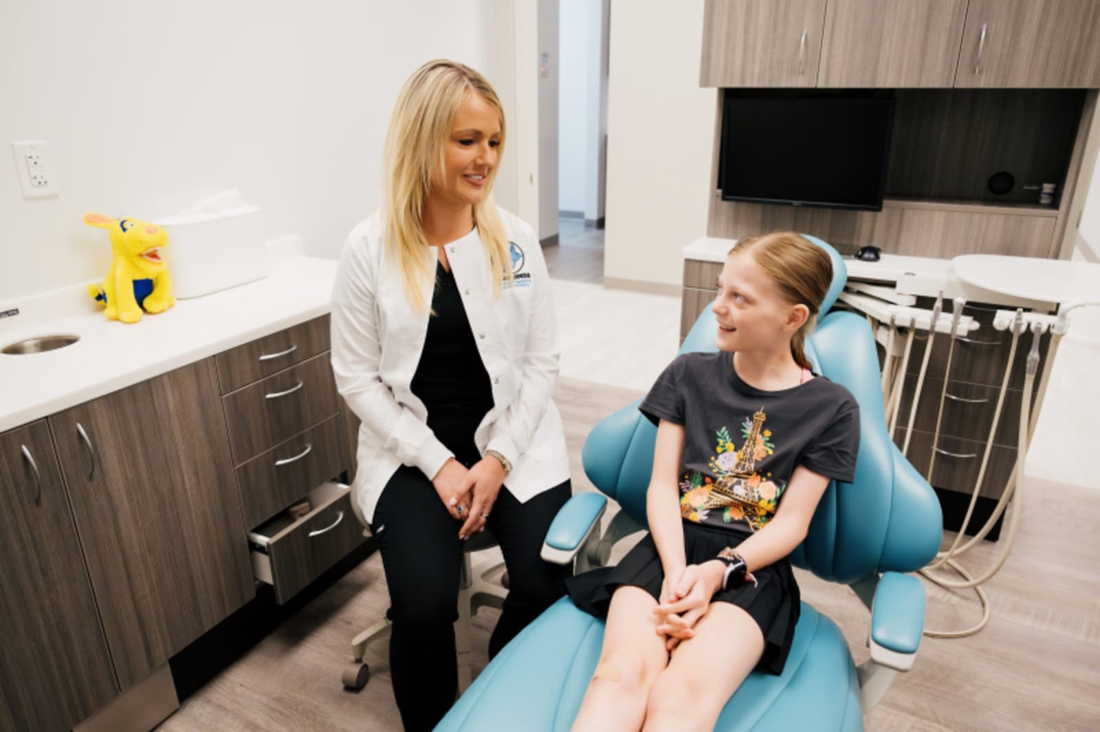 Female dentist in dark clothing speaking with young patient in clinical treatment room