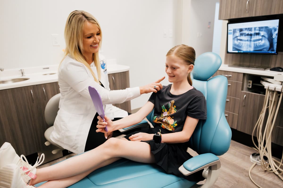 Female dentist in purple scrubs examining a young child patient in the dental chair