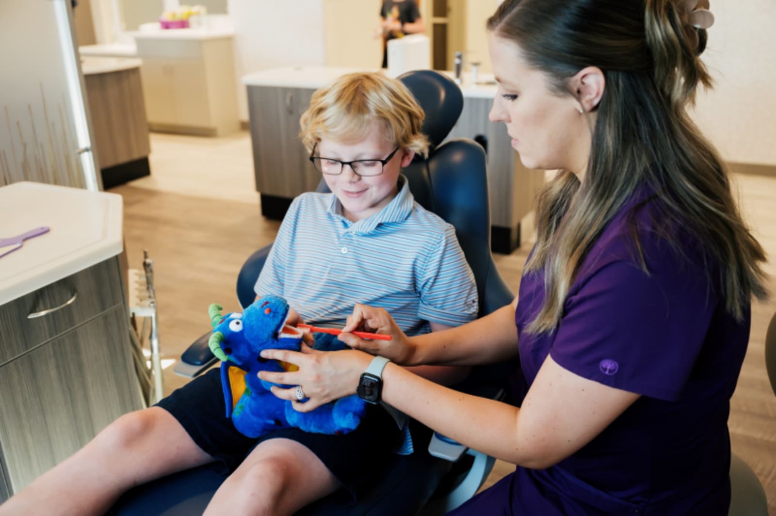 Dentist in purple scrubs showing a young child how to use a dental tool
