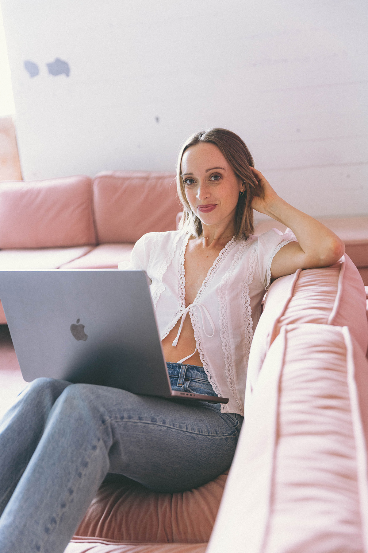 Paige Aileen Web Designer sitting on a pink couch with her laptop