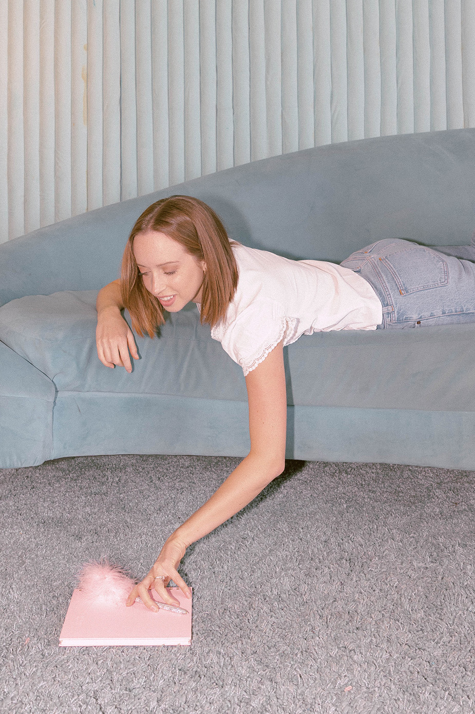 Paige Aileen Website Designer on blue couch reaching for pink notebook