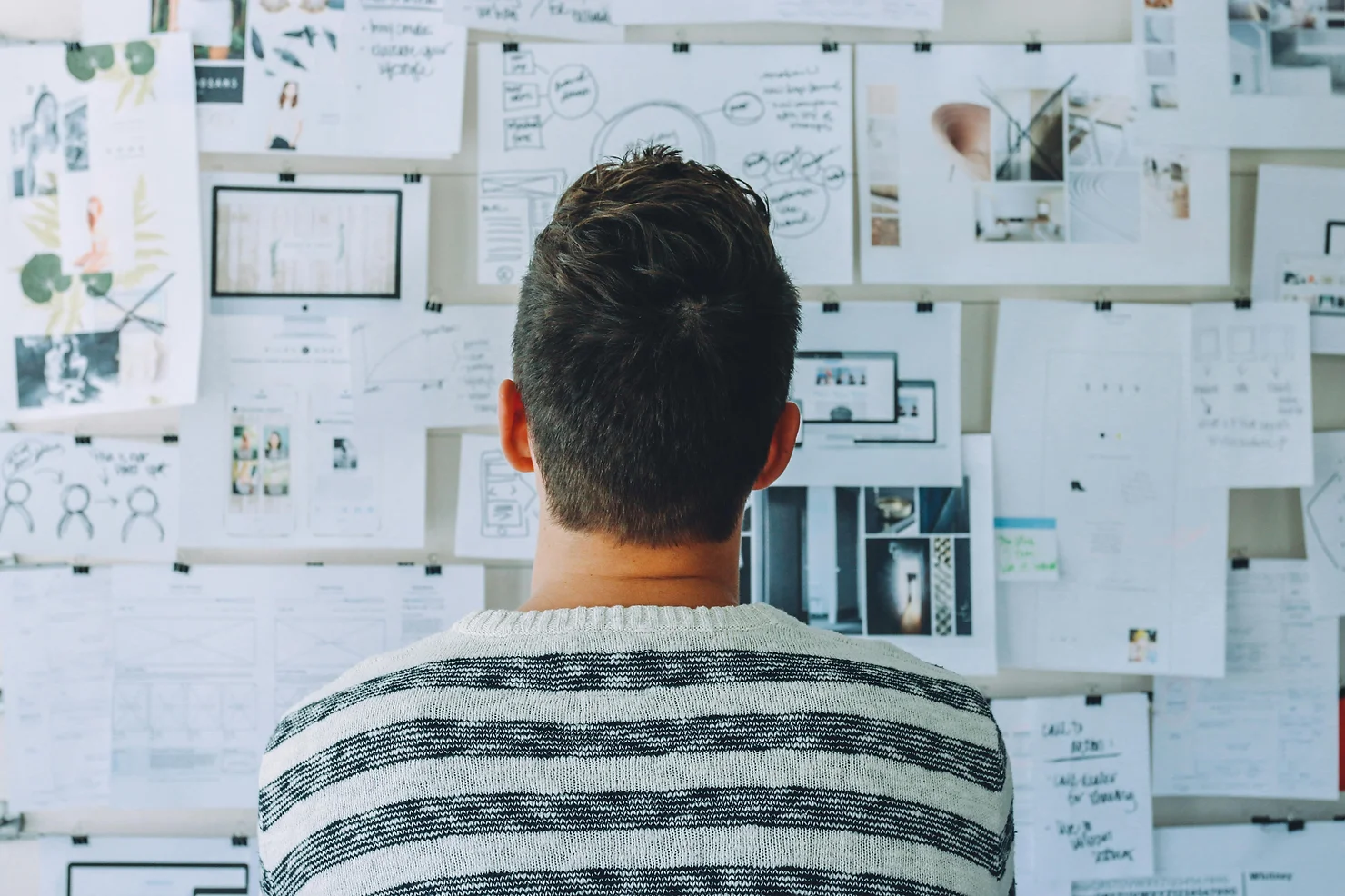 Photo of a man sitting and brainstorming in front of a whiteboard filled with pinned documents