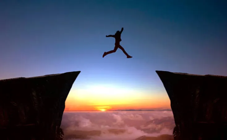 Photo of a man jumping from a high-altitude cliff ledge to another