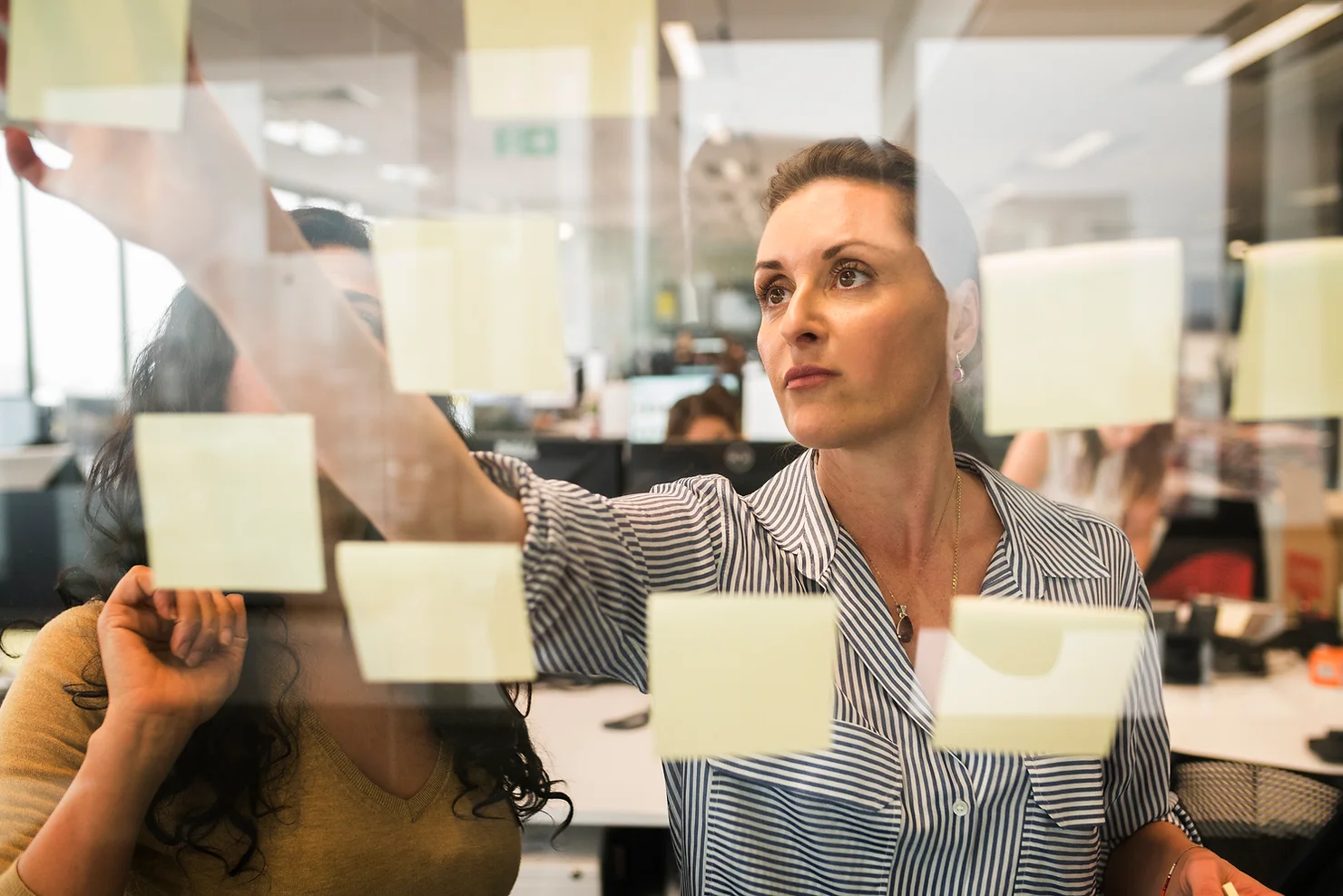 Photo of coworkers workshopping and sticking sticky notes on a glass board