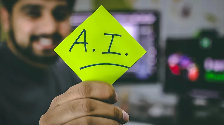 Photo of a man holding a sticky note that says "AI" with an underline, smiling in the background