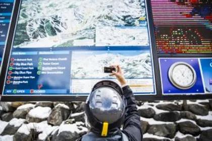 Photo of a man photographing a mountain map in snowy surroundings
