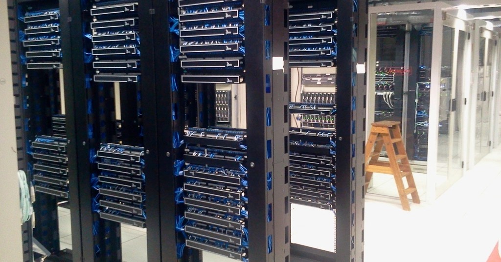 Rows of black server racks with blue network cables in a data center.