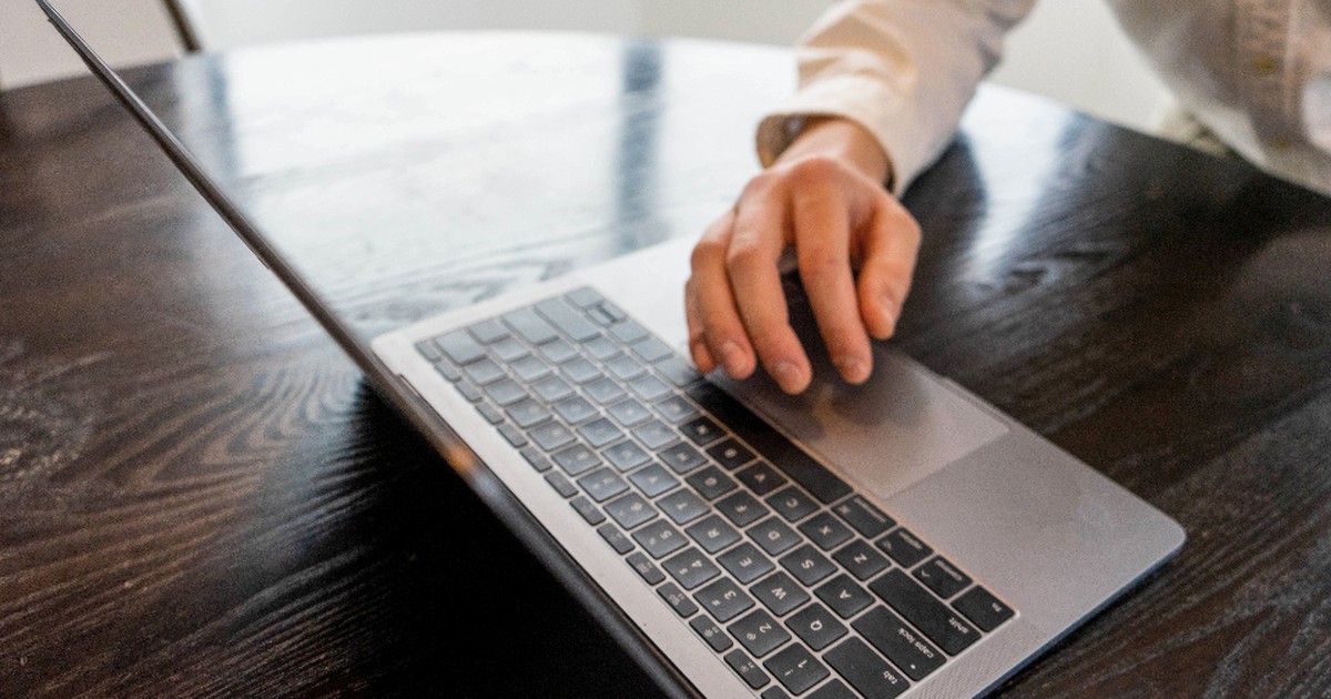 A close-up of a hand typing on a laptop keyboard at a wooden table, the kind of independent digital work platforms like Amazon Mechanical Turk once paid for.