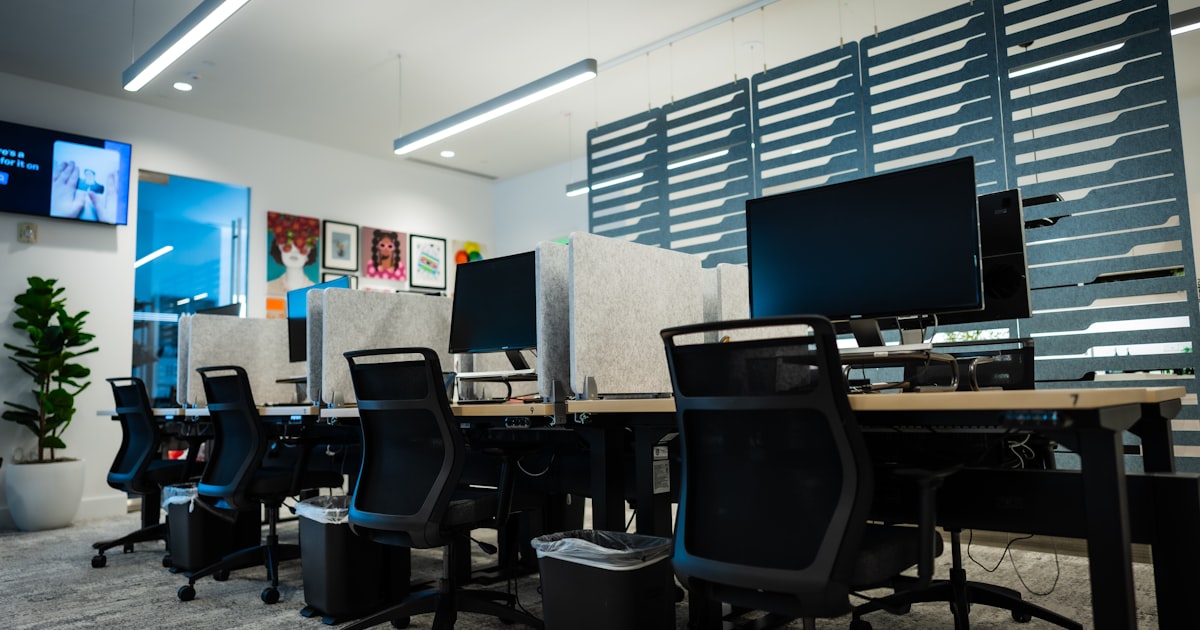 Rows of unoccupied desks with monitors switched on in a modern open-plan office