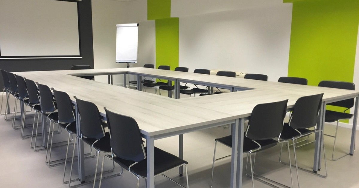 An empty corporate conference room arranged with two rows of vacant black chairs around U-shaped tables, no people present.