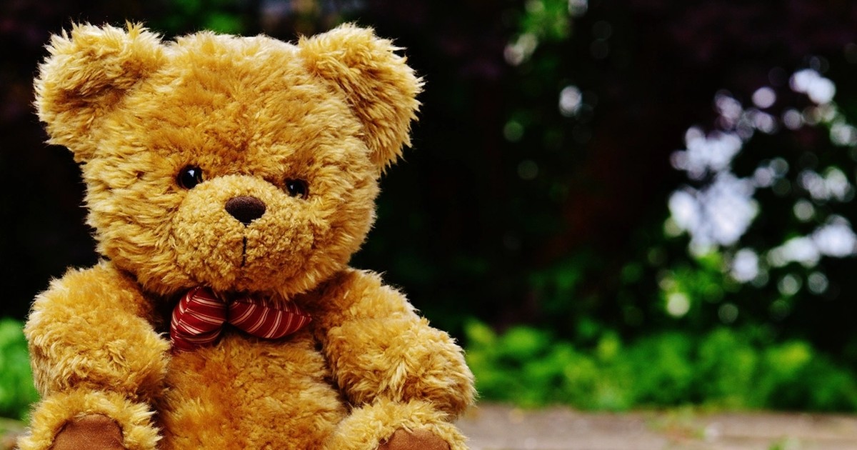 A brown teddy bear with a red bow tie sitting outdoors on a garden path, the kind of plush toy now covered by California's companion-chatbot child-safety law.