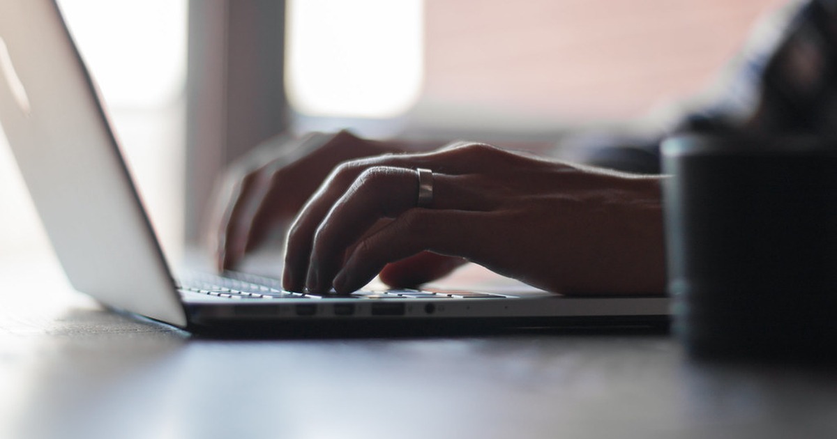 A person's hands typing on a laptop keyboard at a desk, with soft natural light in the background.