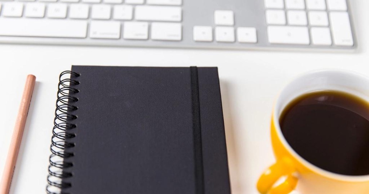A clean office desk with a wireless keyboard, a spiral notebook, a pencil, and a mug of coffee, representing the everyday workplace covered by California's new AI employment laws.
