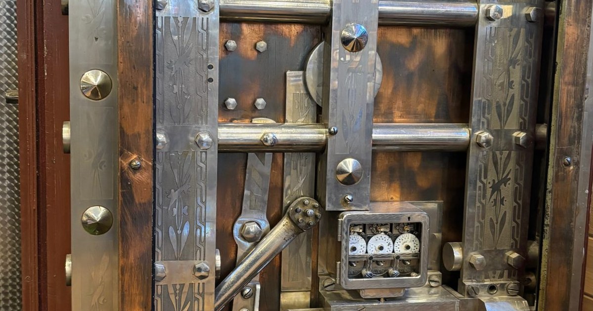 Close-up of an antique bank vault door with riveted steel bars, engraved panels and a combination dial, a closed door to a bank's vault.
