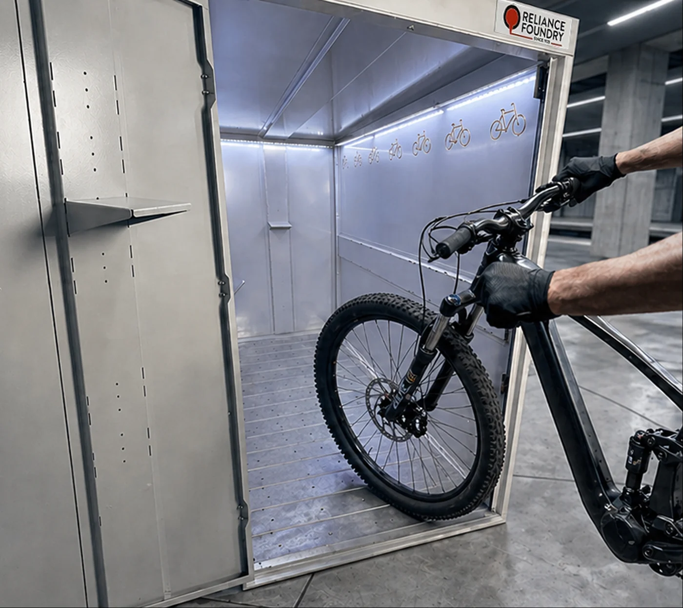 Rider wheeling a bike into a lit Reliance bike locker