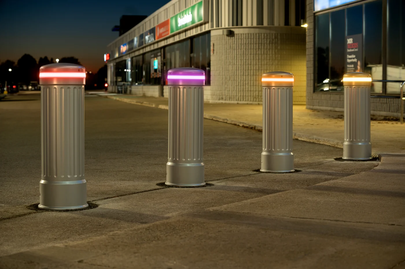 Silver fluted LED bollards outside a strip mall at dusk