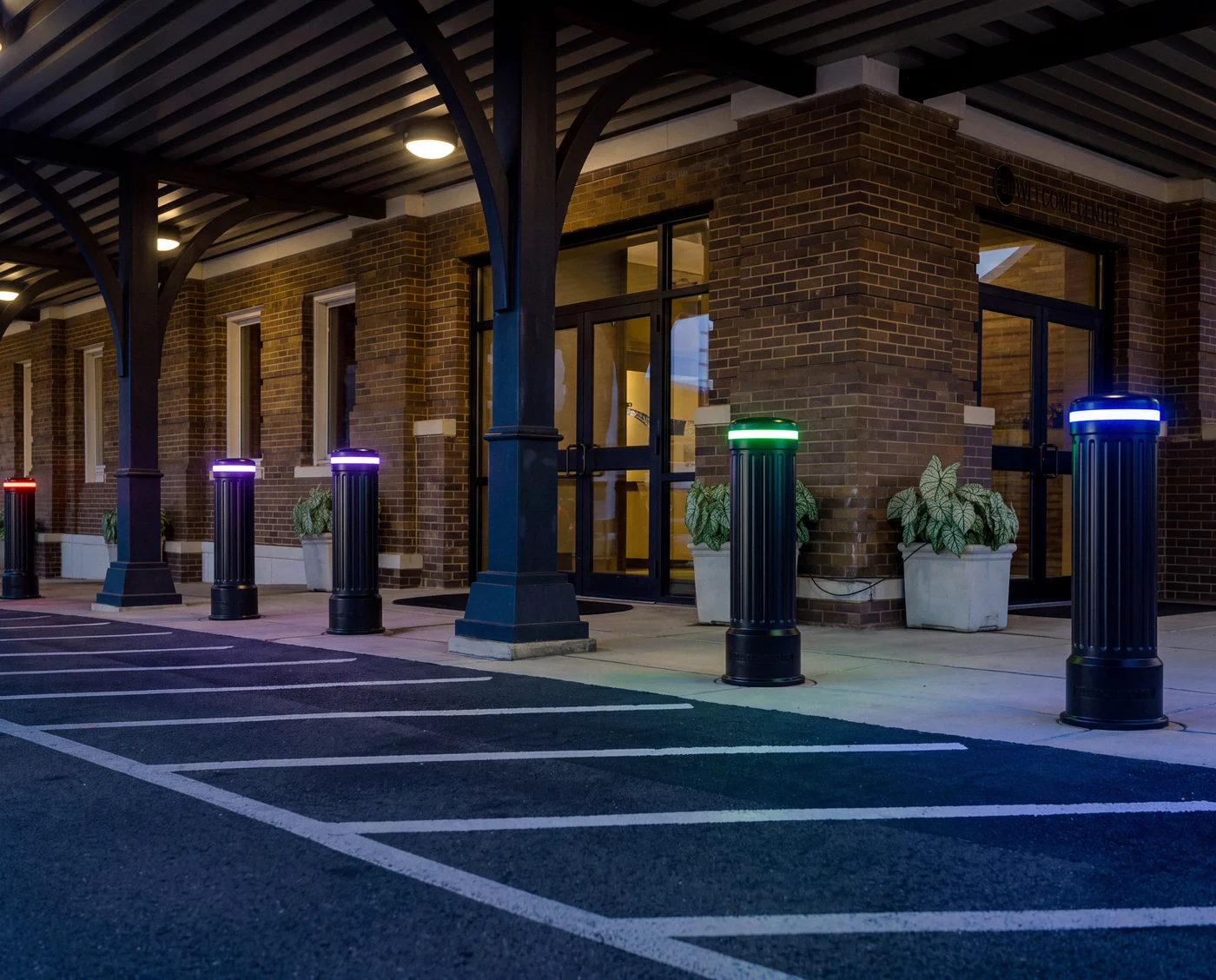 Fluted black LED bollards glowing in different colours outside a brick welcome center at dusk