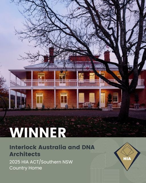 Three-story historic country home called Highclere Farm with brick exterior and white trim, illuminated warmly at dusk with a large bare tree in front, awarded 2025 HIA ACT/Southern NSW Country Home by Interlock Australia and DNA Architects.