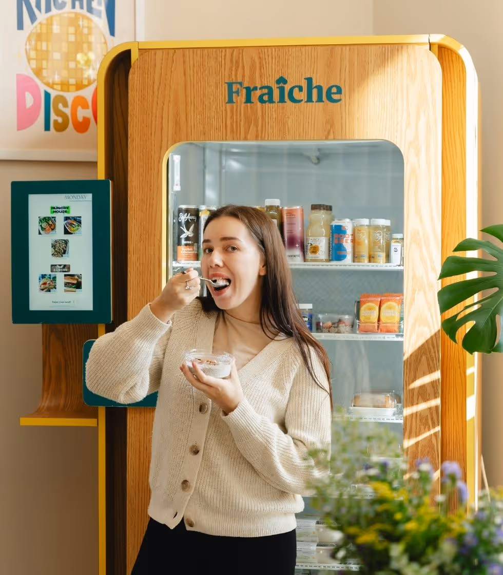 Woman eating healthy snack from office smart fridge