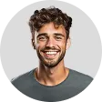 Smiling young man with curly brown hair and beard wearing a gray shirt against a light gray background.