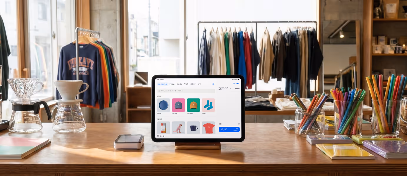 カラフルな服やアクセサリーが並ぶPOSレジアプリの画面をタブレット端末に表示し、周囲に服や文房具、コーヒードリッパーが置かれた幅広い業態で営業しているお店のカウンター。