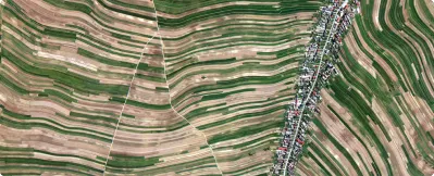 Aerial view of a rural landscape with curved agricultural fields and a village along a road.