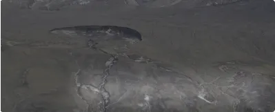 Dark rocky surface with visible fractures and smooth, rounded stones embedded in it.