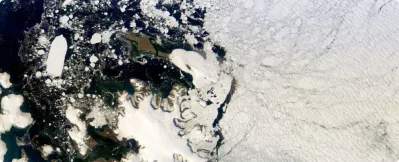 Satellite view of an icy coastline with jagged ice edges meeting dark ocean water and a large expanse of sea ice.