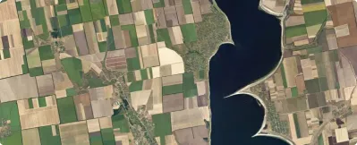 Aerial view of a large body of water bordered by patchwork agricultural fields in varying shades of green and brown.