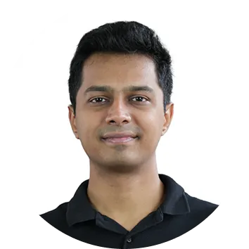 Portrait of a young man with short black hair wearing a black collared shirt, smiling slightly against a white background.