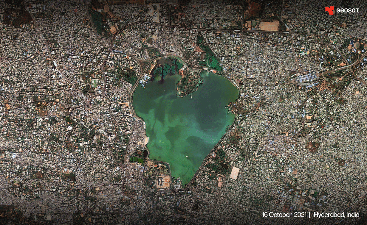 Aerial satellite view of Hyderabad, India, showing a large green-blue lake surrounded by dense urban development.