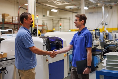 Two business professionals shaking hands in a Rochester Hills IT managed services facility with industrial equipment