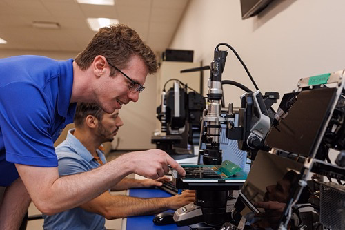 Two IT technicians examining and working on circuit boards using professional diagnostic equipment in a lab