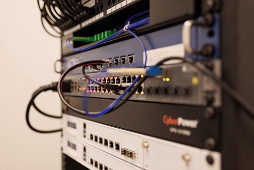 Network rack with patch panel, managed switches, fiber cables, and CyberPower UPS in a Rochester Hills server room