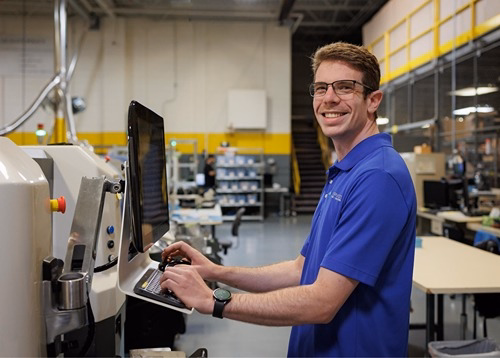 Smiling IT technician operating industrial manufacturing equipment control panel in a Rochester Hills facility