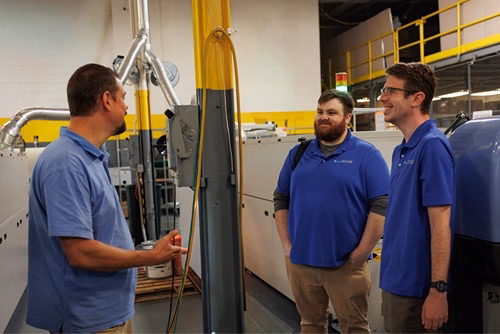 Three IT professionals in blue polo shirts discussing managed IT services and solutions in a technology facility