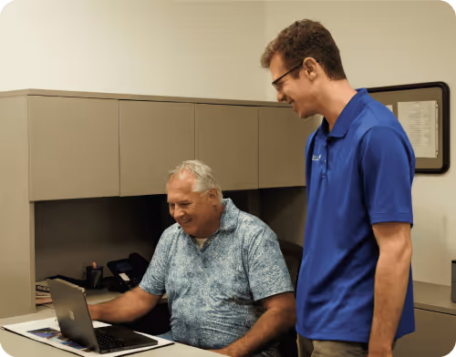 Leet IT technician assisting business owner with managed IT support on laptop at office desk in Rochester Hills