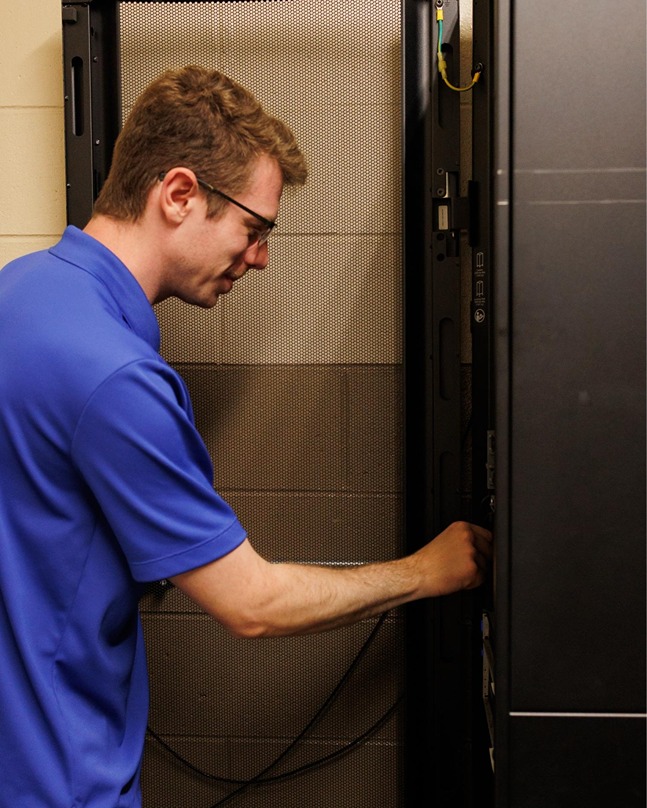 IT technician in blue polo configuring server rack equipment in a data center