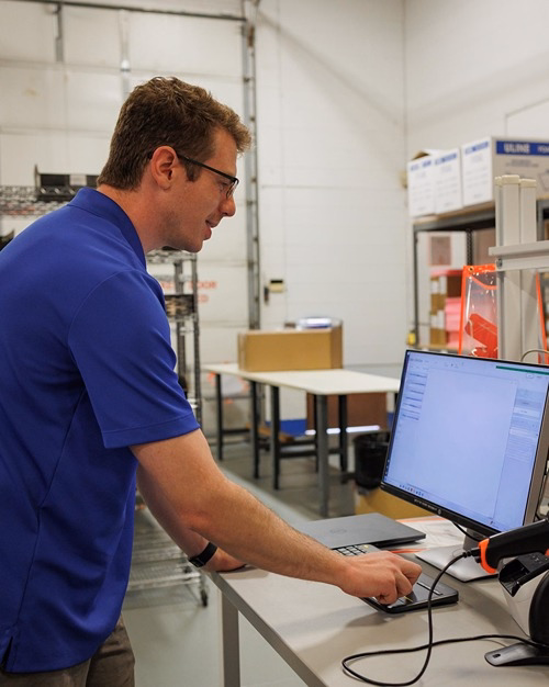 IT technician in blue polo reviewing network management software on monitor in warehouse workspace