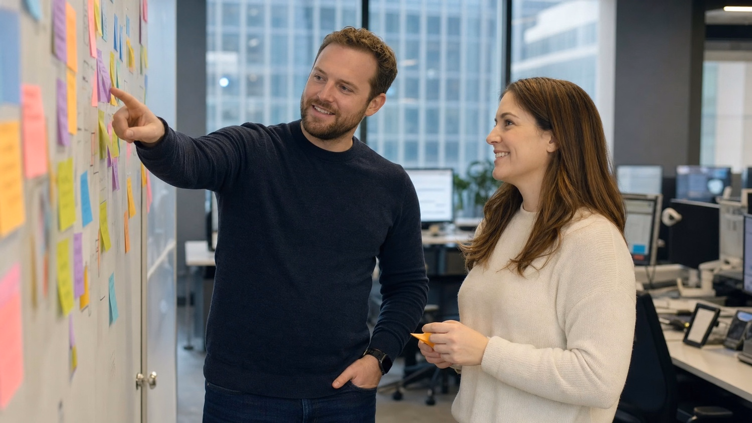 Two Caucasian individuals in their 30s, wearing casual business attire, stand ne