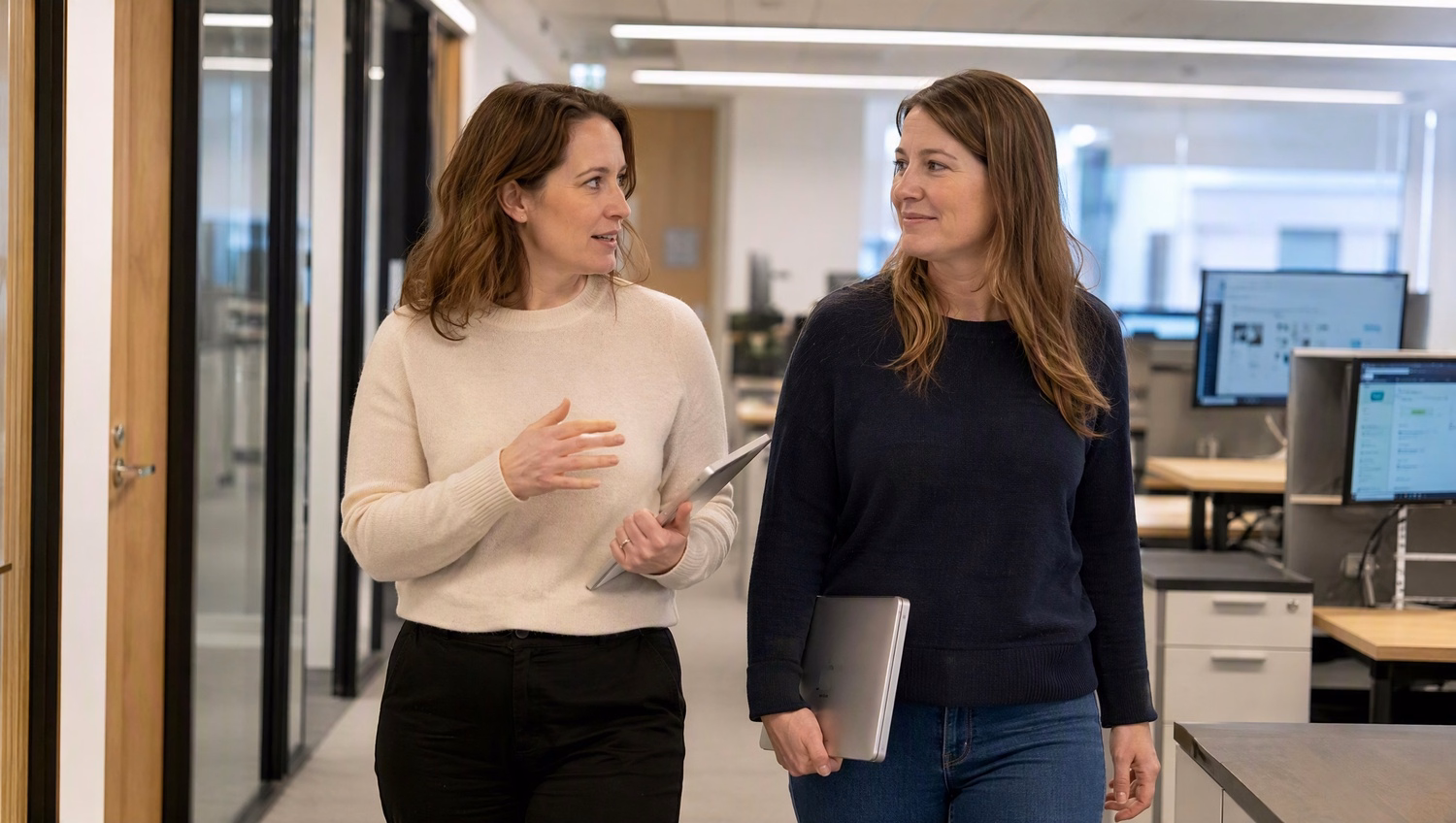 Two women in office hallway discussing serious business