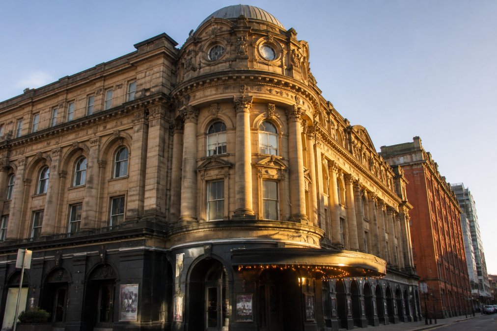 Historic Victorian music venue exterior with ornate stonework and vintage theatre signage, golden afternoon light casting shadows across the facade