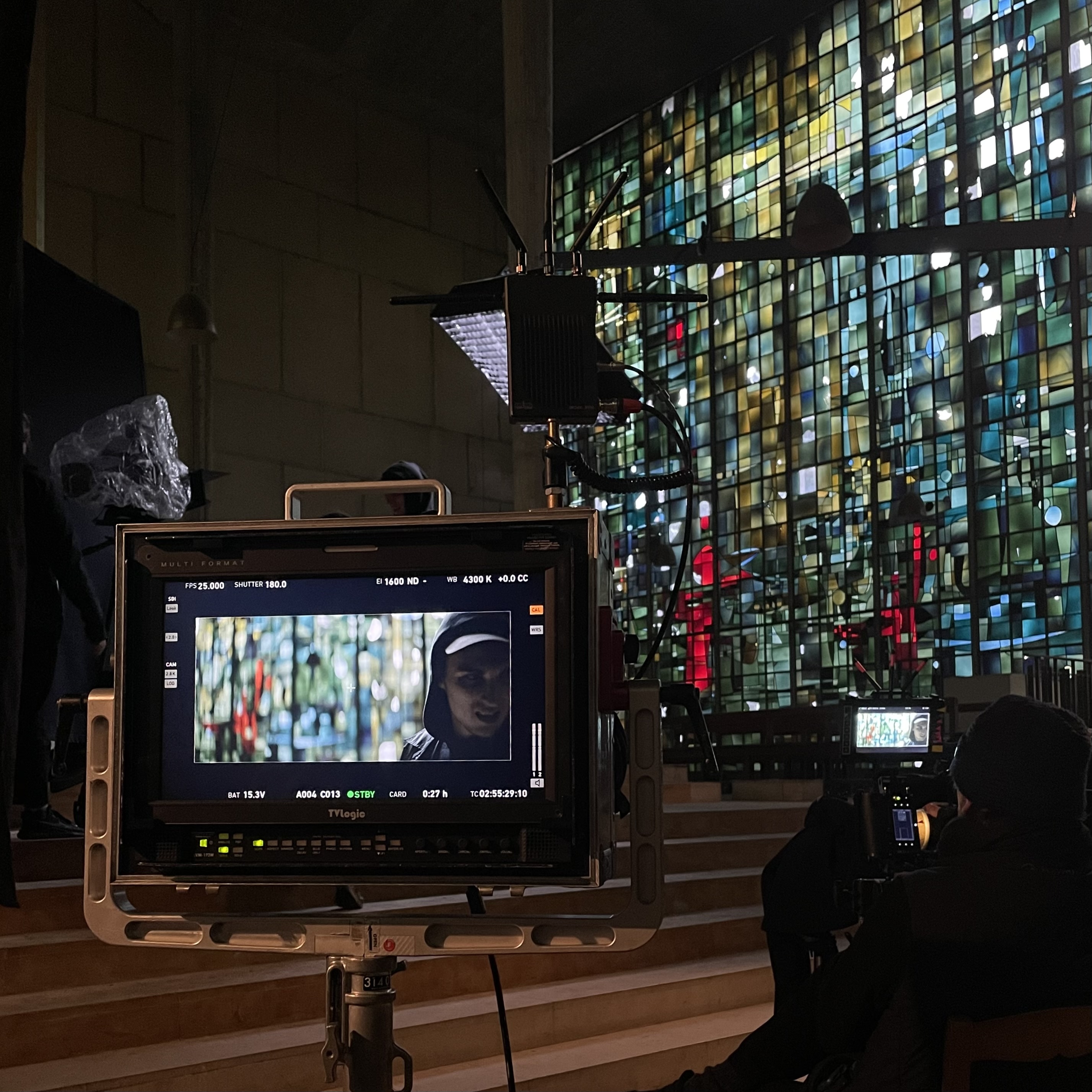 Film crew at work in a church location in France, with a stained glass window in the background and a monitor showing the shot of a hooded subject, showcasing the work of Fixer France on set