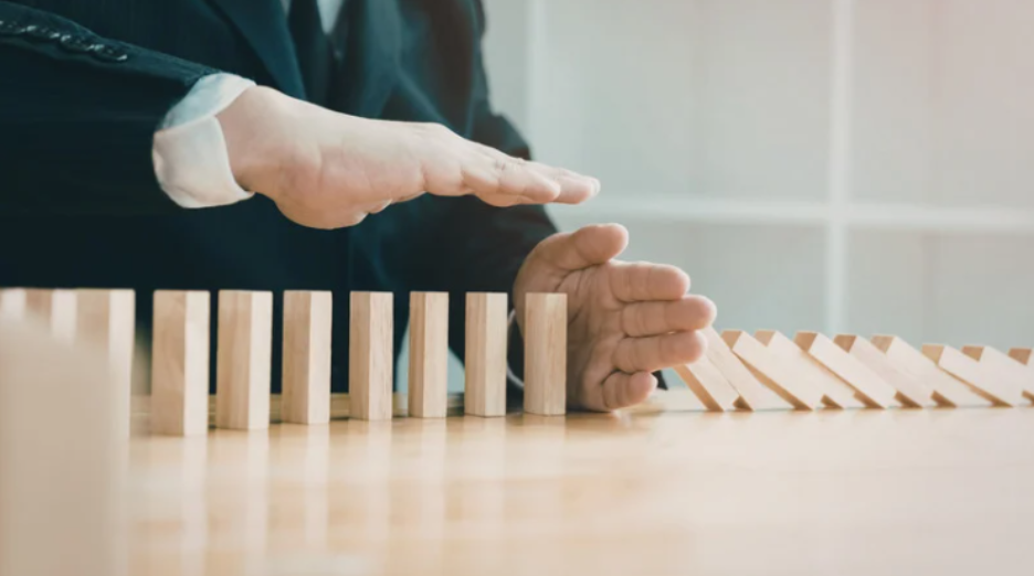 Hands stopping falling dominoes, representing decision making in leadership 