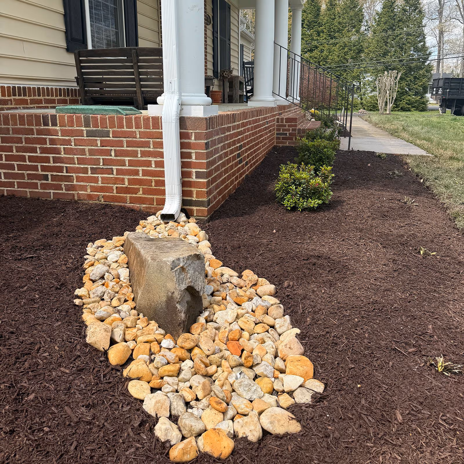 Fresh mulch along with rocks decorating a drainage downspout by Larsen's Lawn and Landscape.