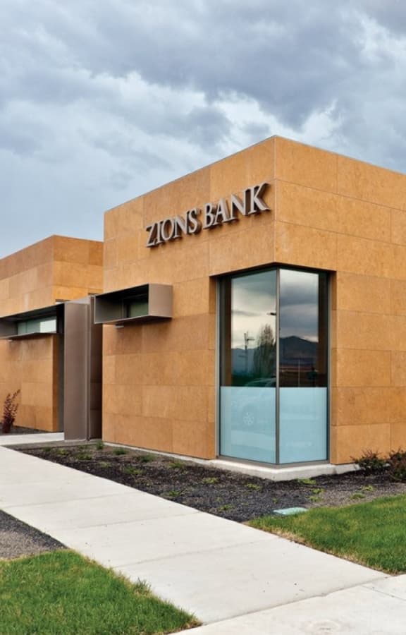 Modern Zions Bank building with tan exterior walls and large windows under a cloudy sky.