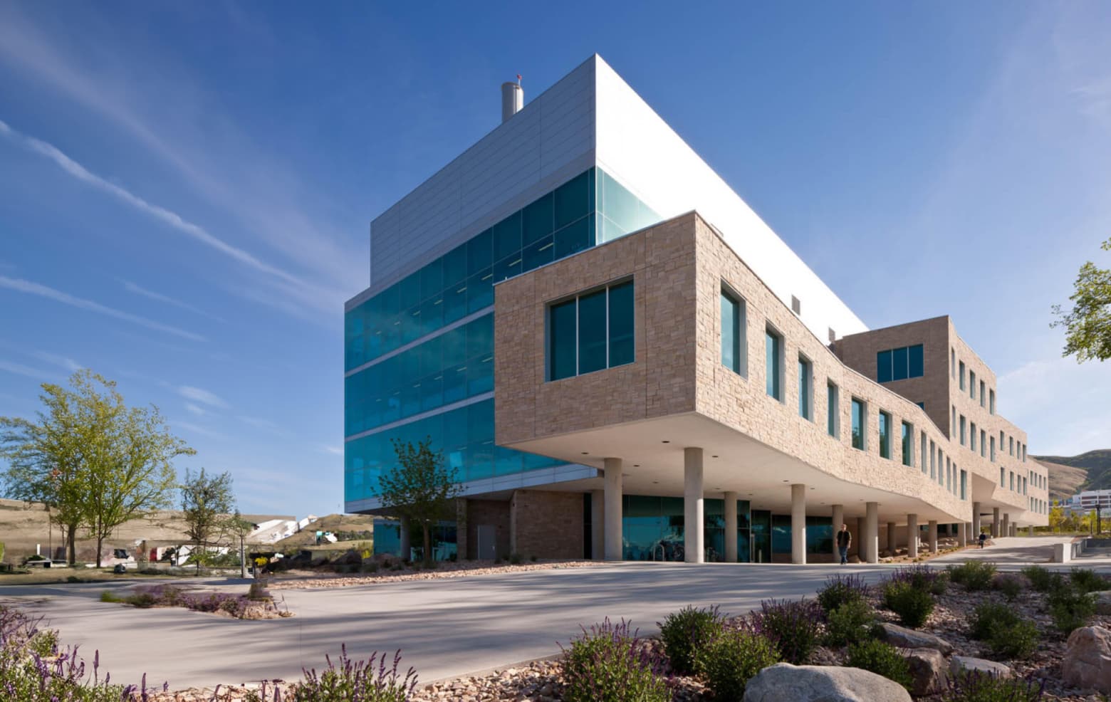 Modern multi-story building with glass and stone facade under a clear blue sky.